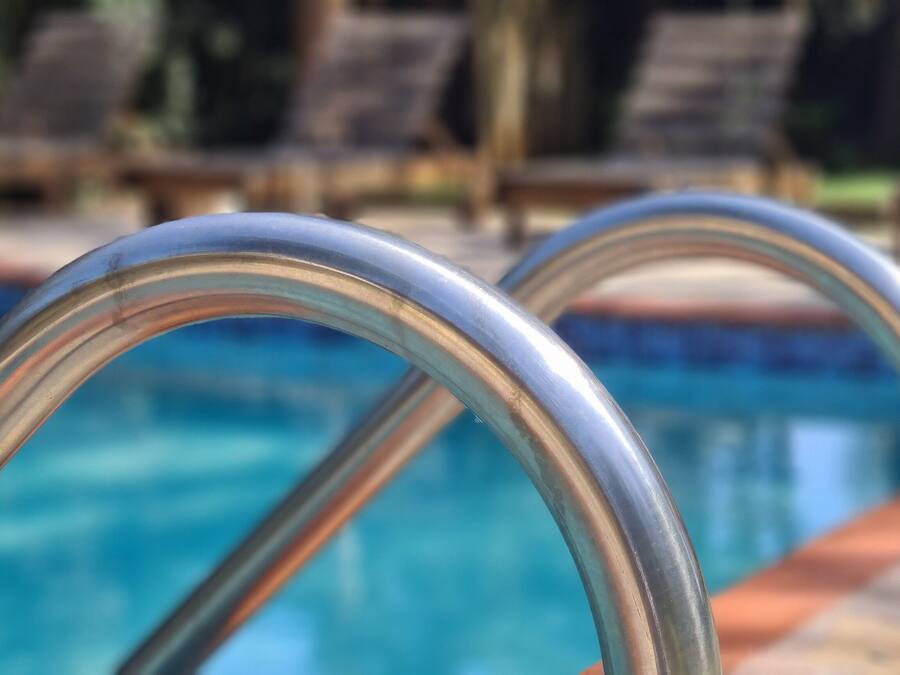 Una piscina con barandillas de metal y sillones de descanso al fondo.