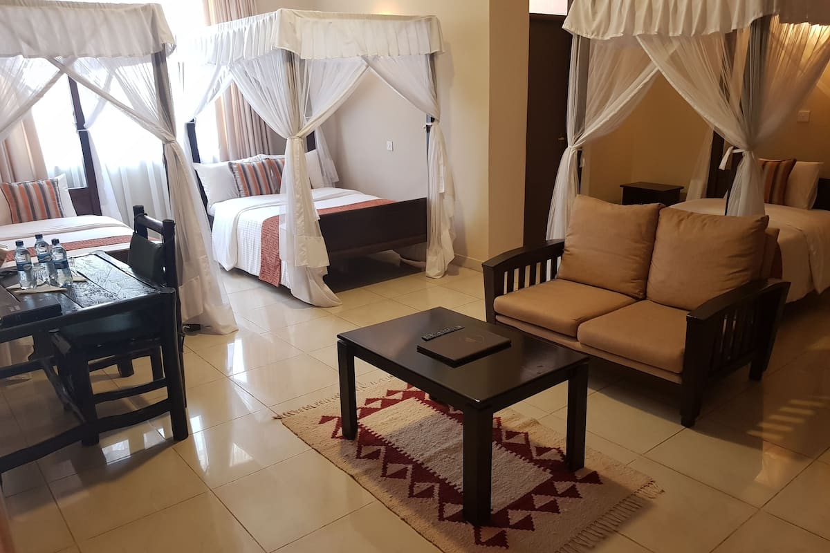 A hotel room with a bed, a sofa, a coffee table, and a dining table with chairs.