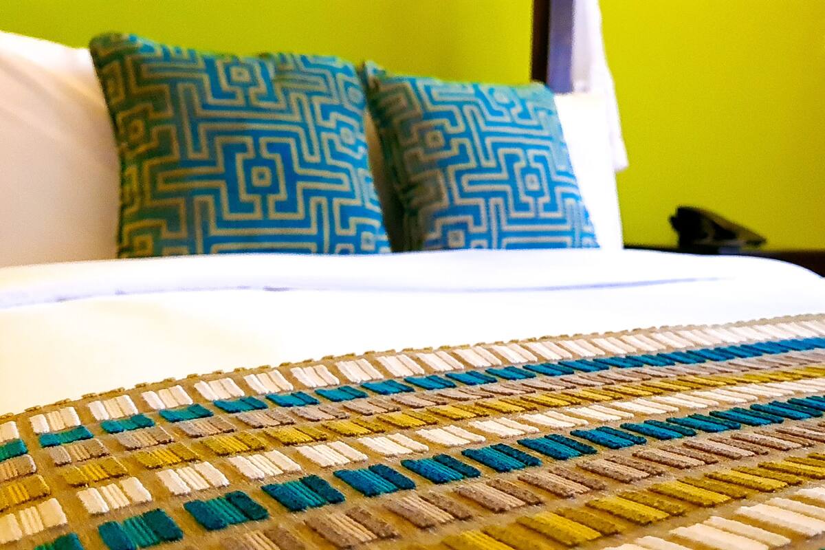 A bed with a patterned bedspread, two pillows with a geometric design, and a green wall in the background.