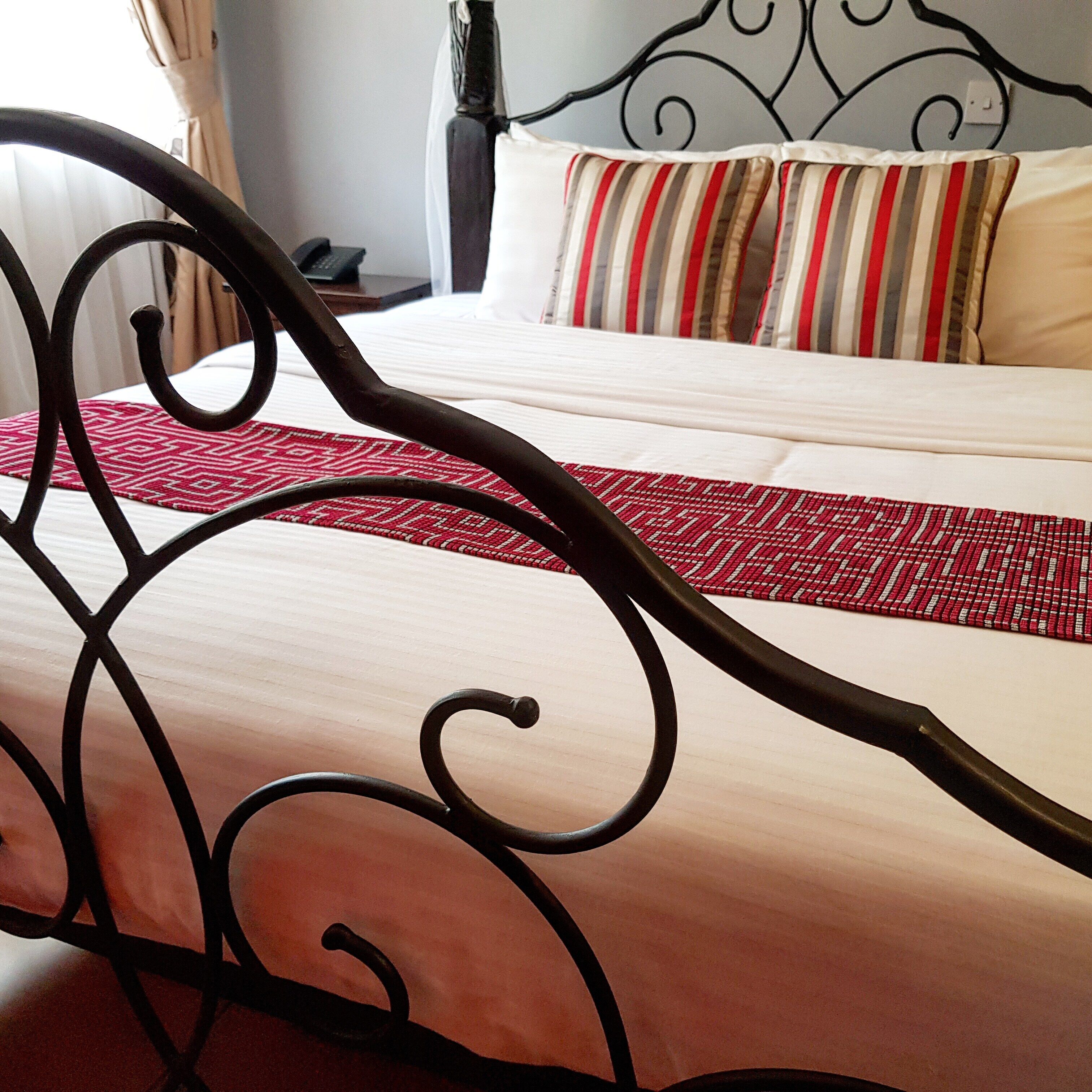 A bed with a red and white patterned bedspread, a black metal headboard, and a white pillow with red stripes.