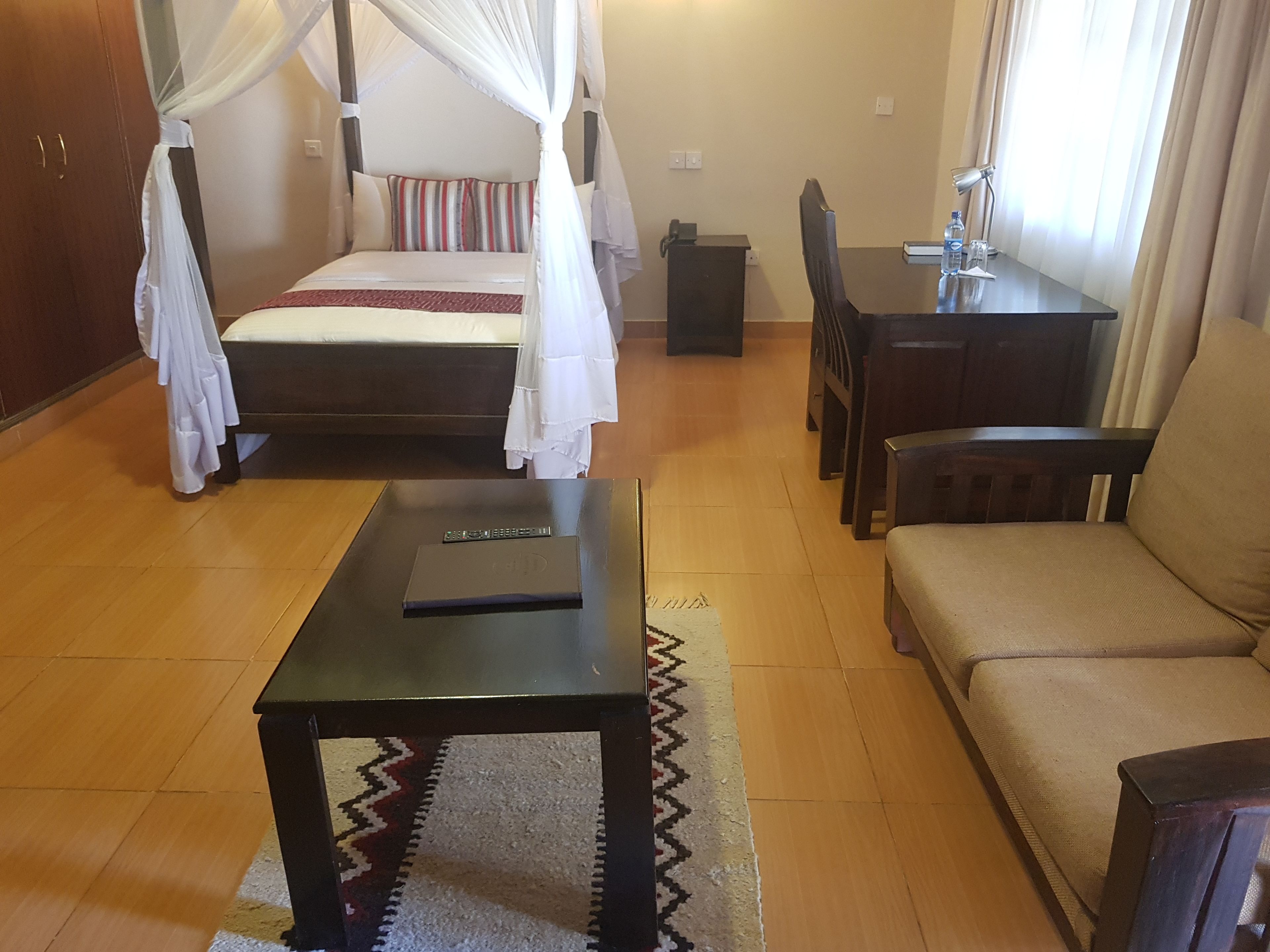 A bedroom with a four-poster bed, a bedside table, a sofa, a desk with a chair, and a small rug.