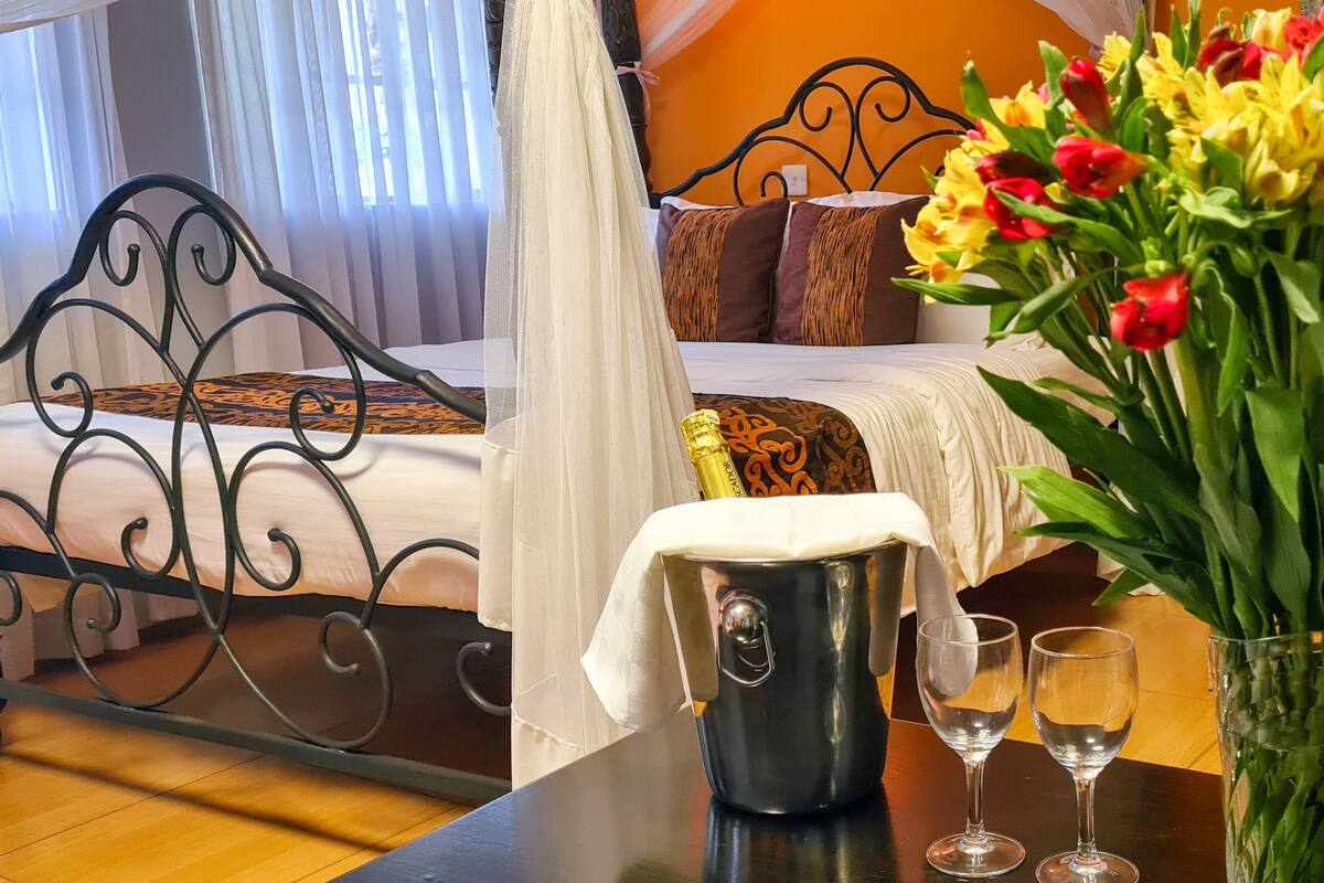 A bedroom with a bed, a nightstand, a vase of flowers, and a bottle of champagne.
