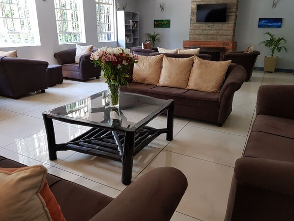 A modern living room with a glass coffee table, brown sofas, and a fireplace.