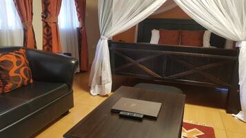 Ein Zimmer mit einem dunklen Holzbett, einem schwarzen Ledersofa mit einem orangefarbenen Kissen und einem Holztisch mit einem Laptop.
