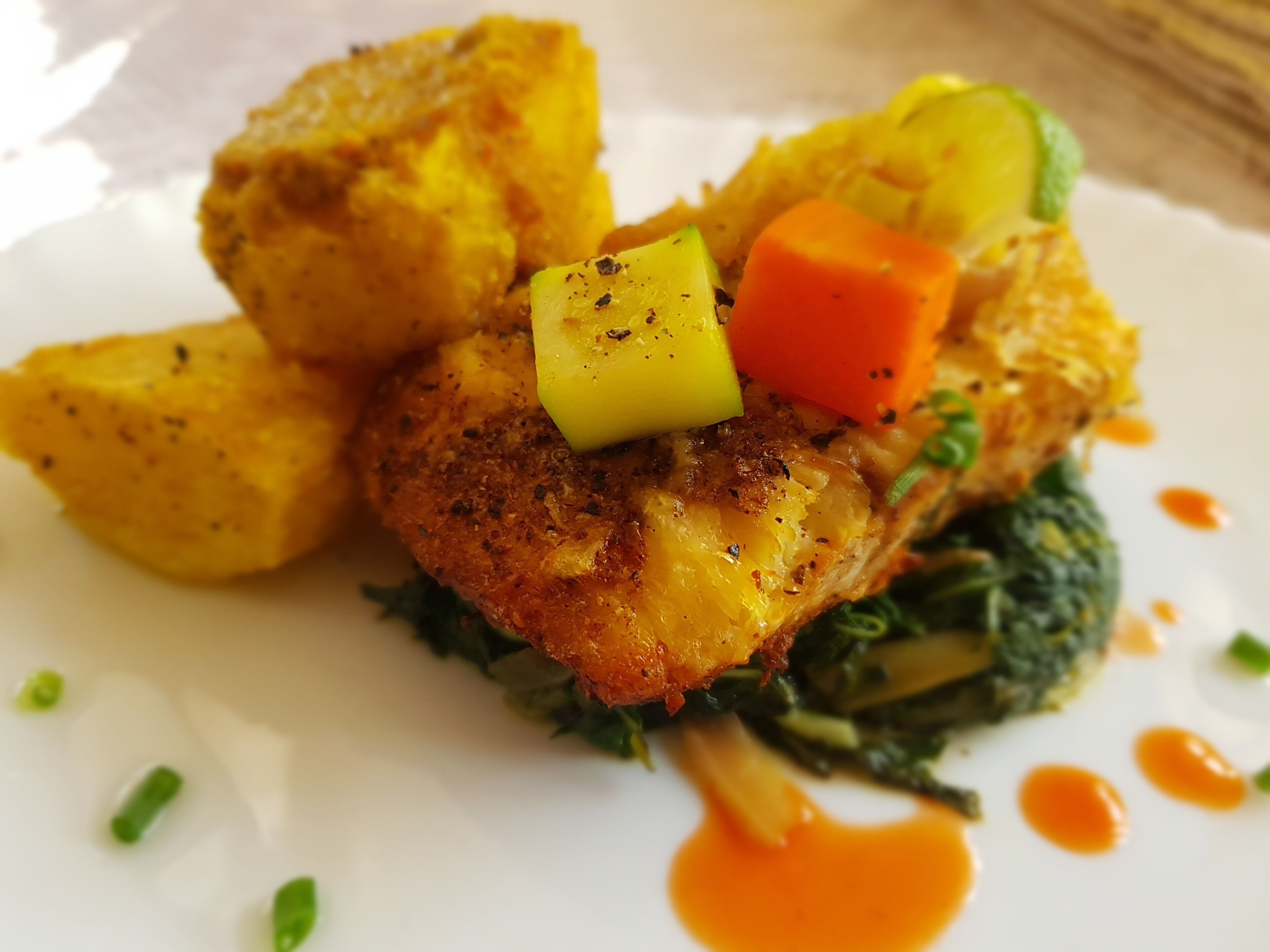 A plated dish with a golden-brown crust, diced vegetables, and a sauce.