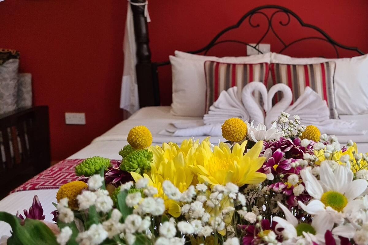 A neatly made bed with white linens and a decorative swan pillow arrangement. A large floral centerpiece adorns the bed, featuring yellow and white flowers.