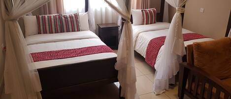 Habitación de hotel con dos camas, cada una con dosel, una mesita de noche y una silla.