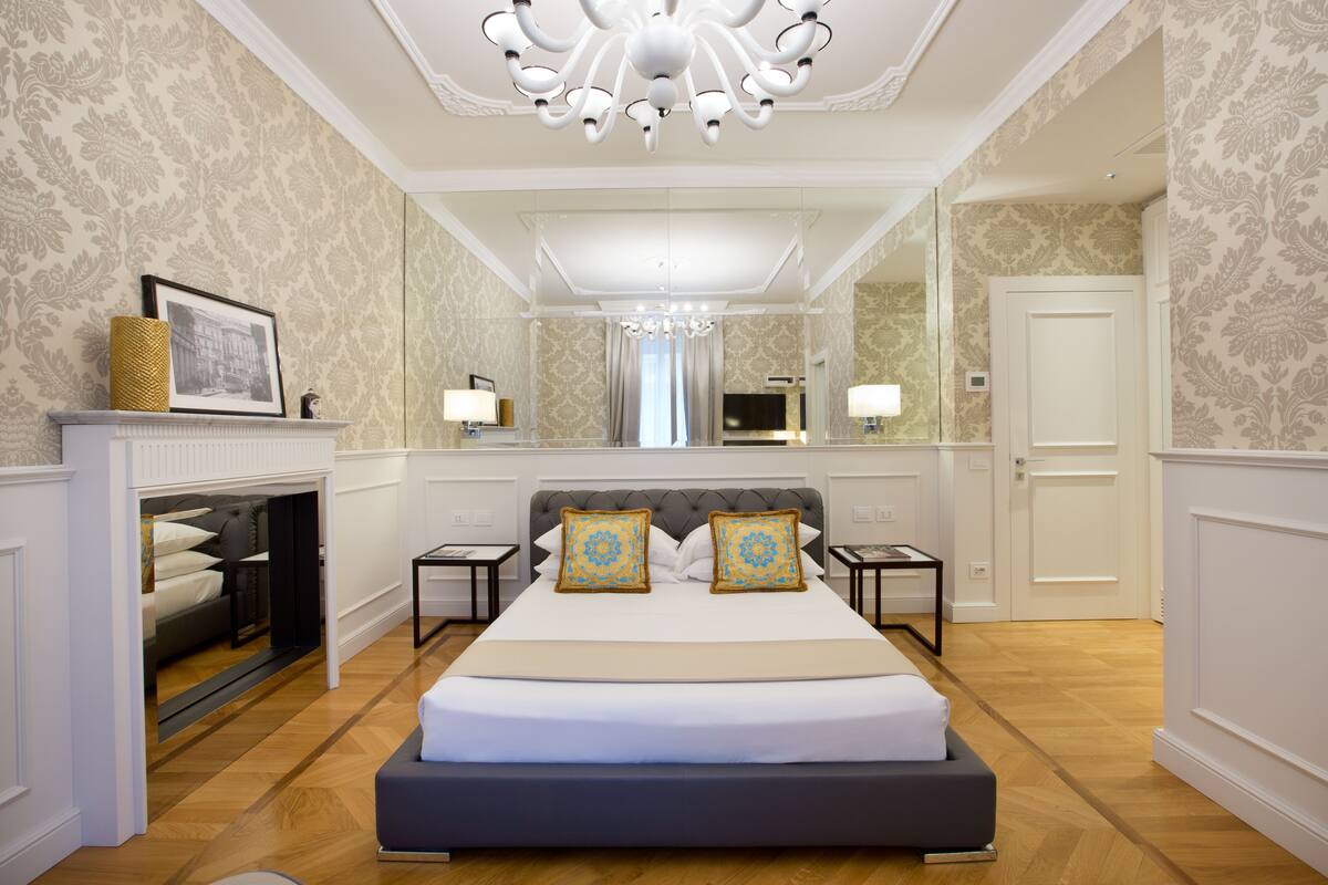 A spacious bedroom with a large bed, a fireplace, a television, and a mirror.