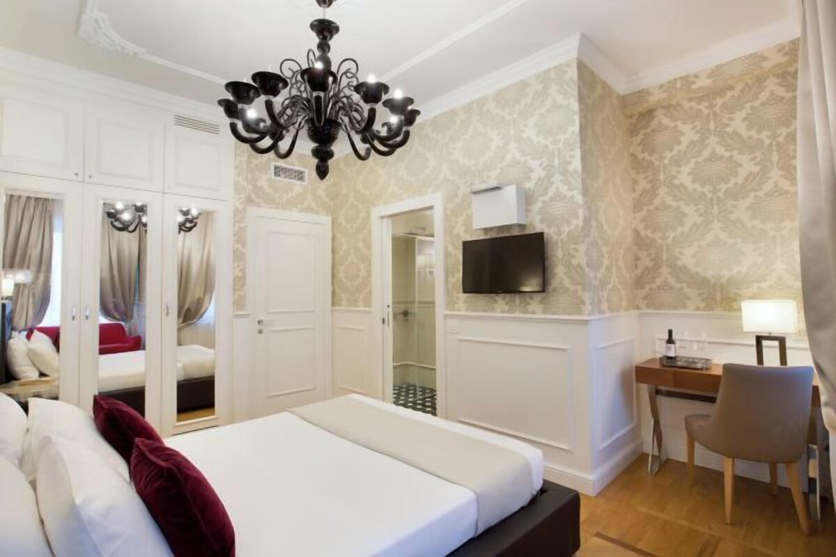 A hotel room with a bed, a desk, a chair, a TV, and a shower area.