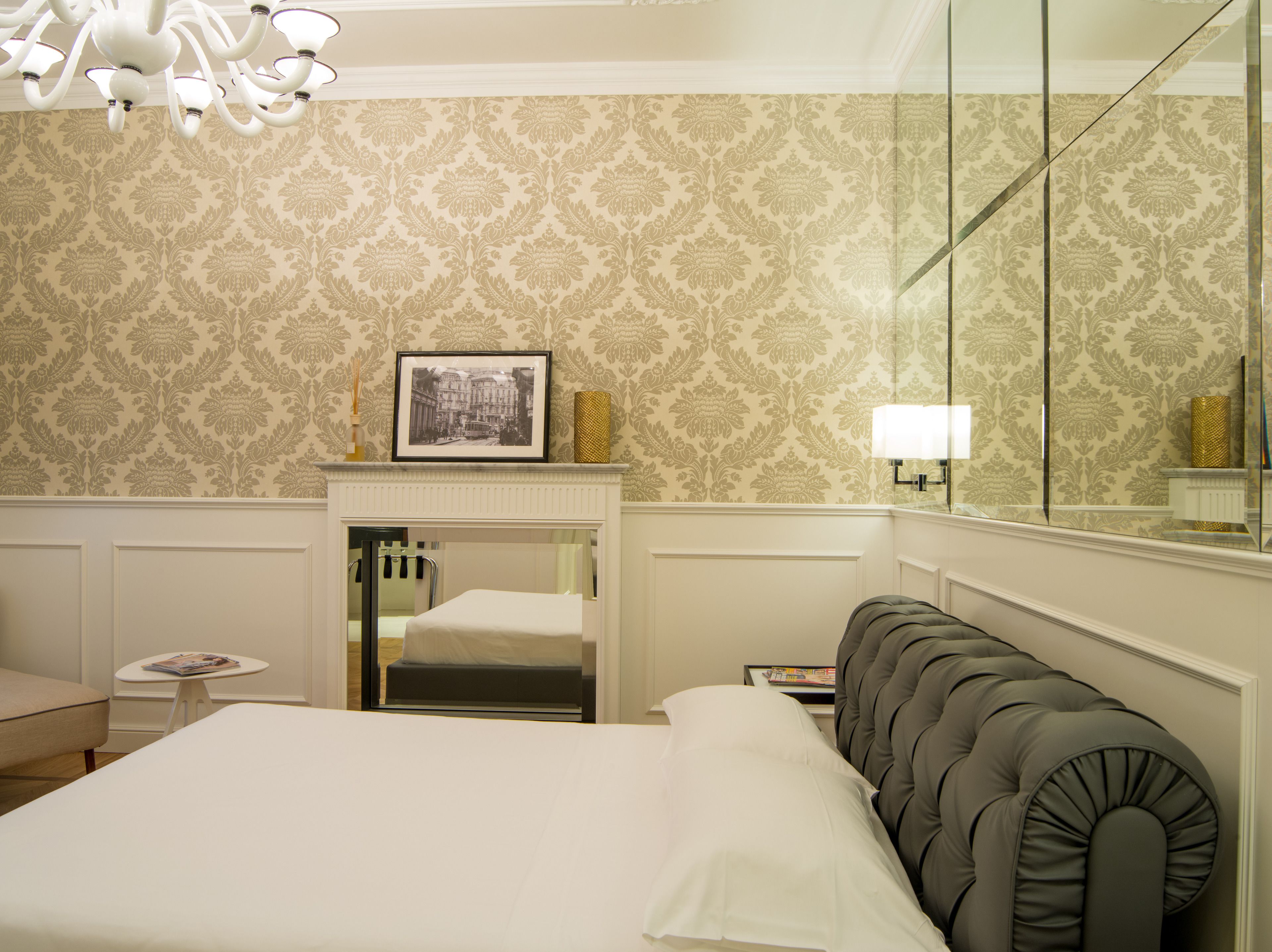 Una habitación de hotel con cama, una mesita, una silla, un espejo y una araña.