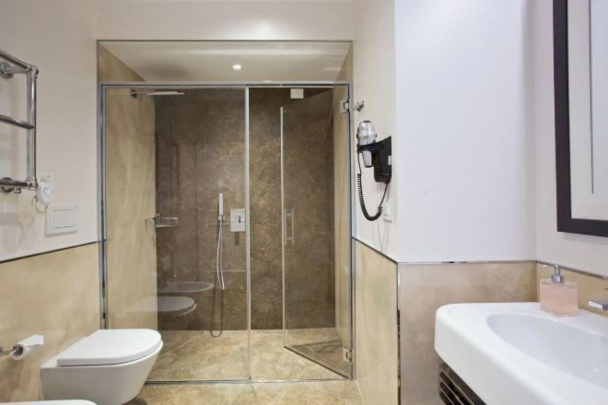 A modern bathroom with a glass-enclosed shower, a white toilet, and a large white sink.