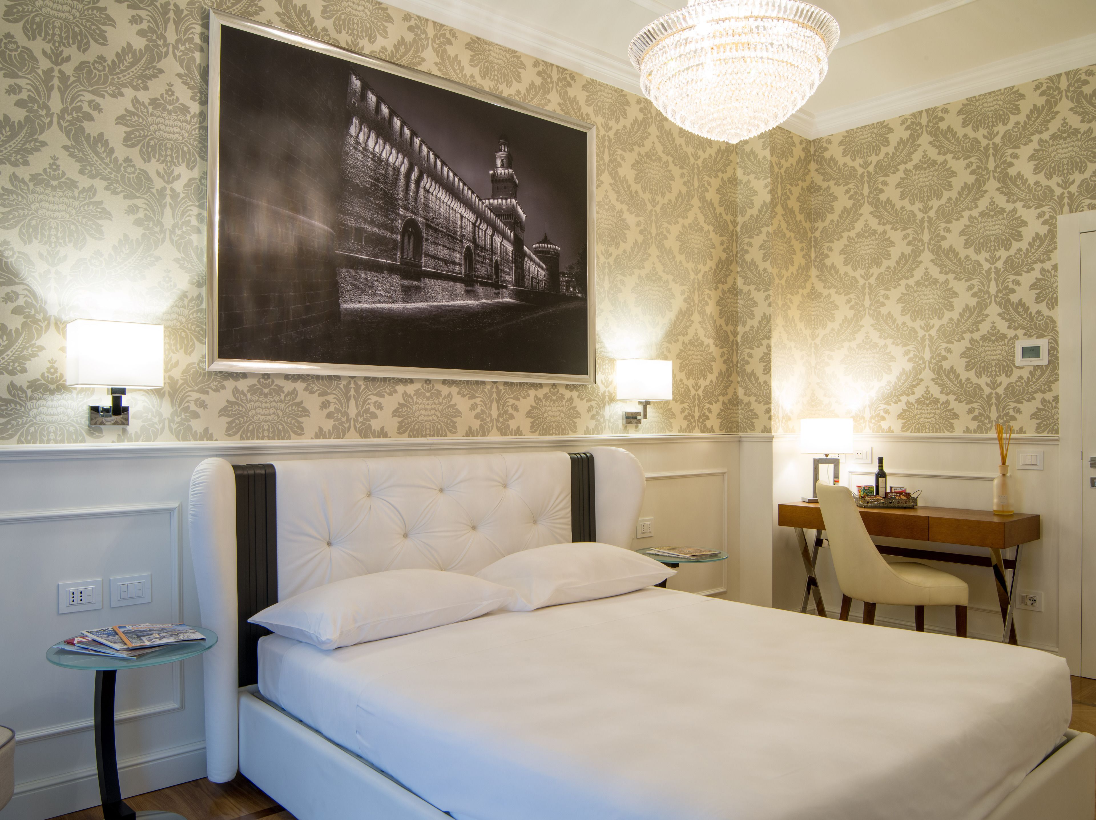 Una camera d'albergo con un letto grande, una scrivania, una sedia, una lampada e un quadro appeso al muro.