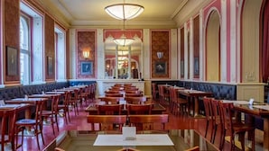 Une salle à manger élégante, avec de longues tables et des chaises, des décorations murales raffinées et un lustre.