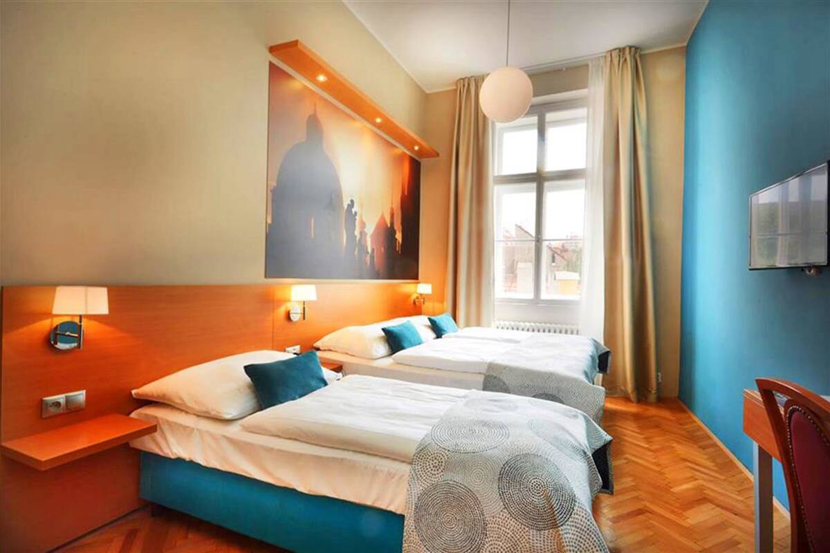 A hotel room with two beds, a large window, a painting on the wall, and a TV mounted on the wall.