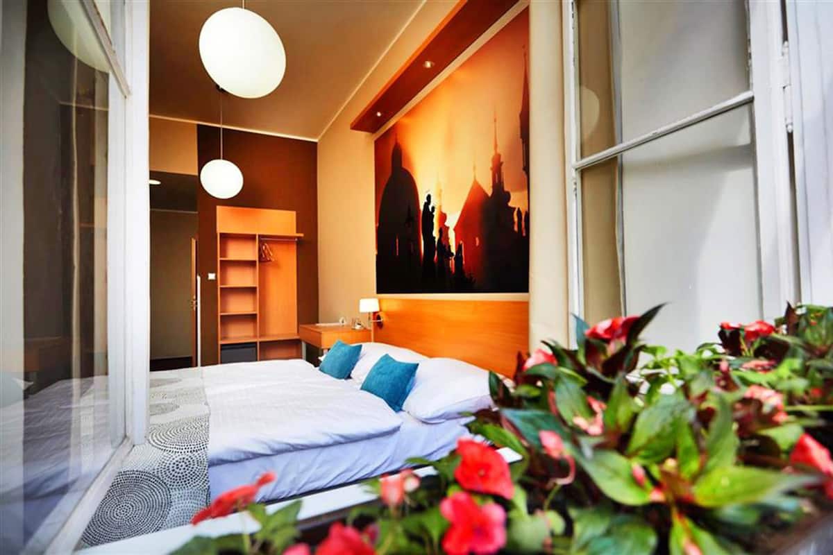 A modern hotel room with a large bed, a cityscape mural, a bedside table, and a window with a view.