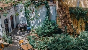 Un espace extérieur aménagé avec des tables et des chaises, entouré de verdure et d’un arbre.