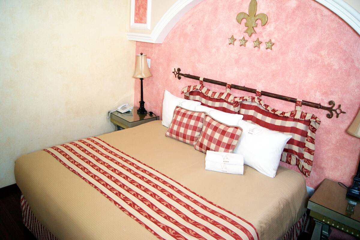 A neatly made bed with a checkered pillow and a headboard with a fleur-de-lis symbol.