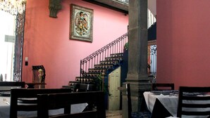 A dining area with tables set for service, a staircase, and a decorative wall piece. - Villahernan Hotel (Puebla)