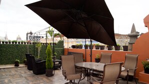 An outdoor patio with a table and chairs, surrounded by potted plants and a large umbrella. - Villahernan Hotel (Puebla)