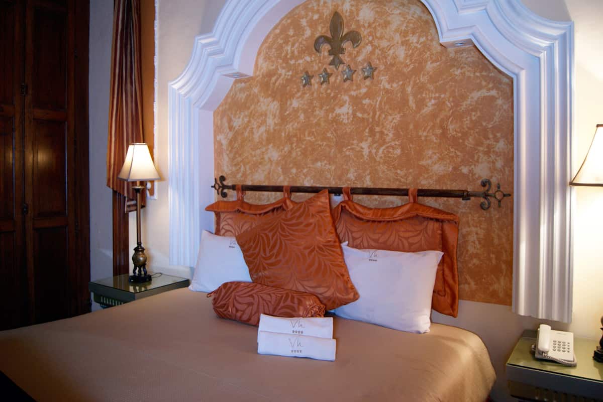 A hotel room with a large bed, a wooden wardrobe, a nightstand with a lamp, and a telephone.
