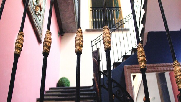 A staircase with ornate black balusters and a pink wall. - Villahernan Hotel (Puebla)