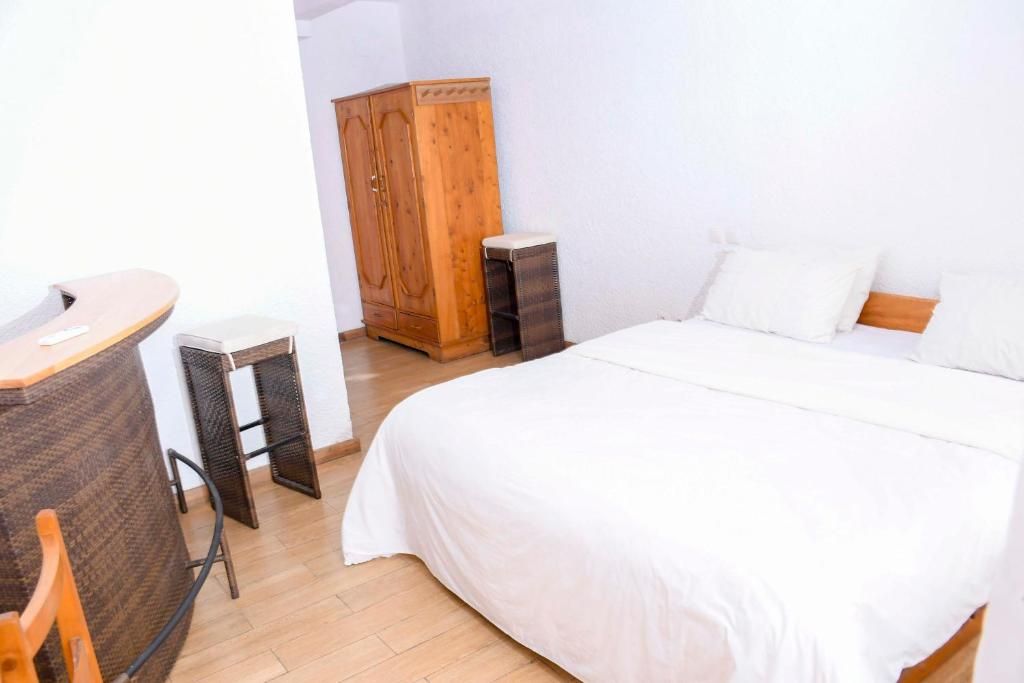 A bedroom with a bed, a wooden wardrobe, a small table, and a chair.