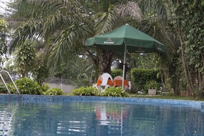 A swimming pool with a Heineken branded umbrella, surrounded by lush greenery and a palm tree. - Kiriri Residence Hôtel (Bujumbura)