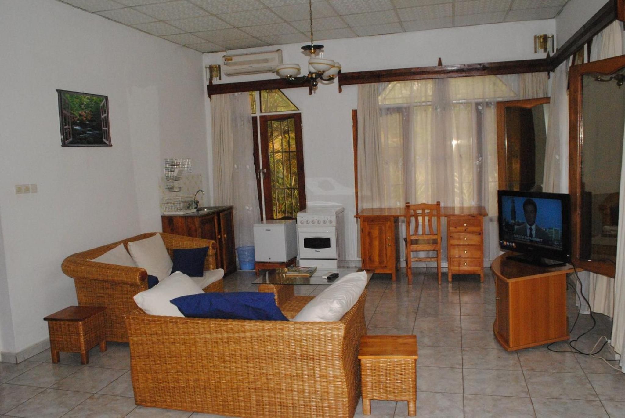 Sala de estar com sofá de vime, televisão, mesa pequena e área de cozinha com fogão.