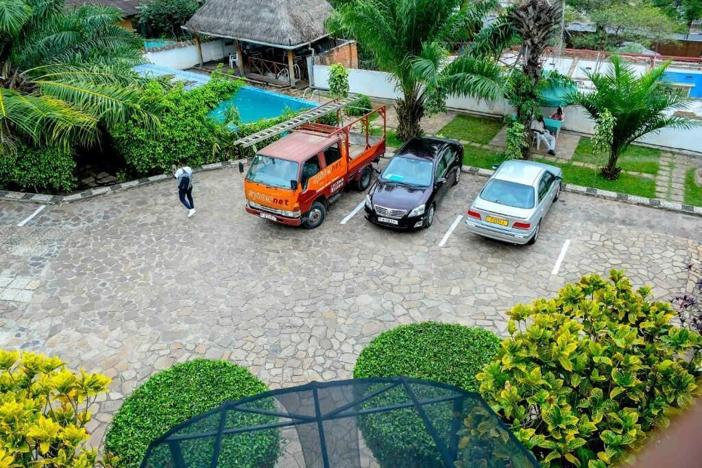A parking area with a stone-paved surface, a red van, a black car, and a silver car parked.