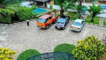 A parking area with a stone-paved surface, a red van, a black car, and a silver car parked.