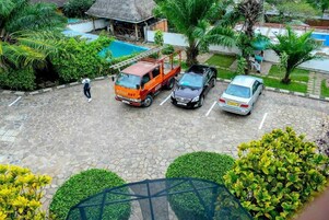Un área de estacionamiento con superficie de adoquines, una camioneta roja, un coche negro y un coche plateado estacionados.