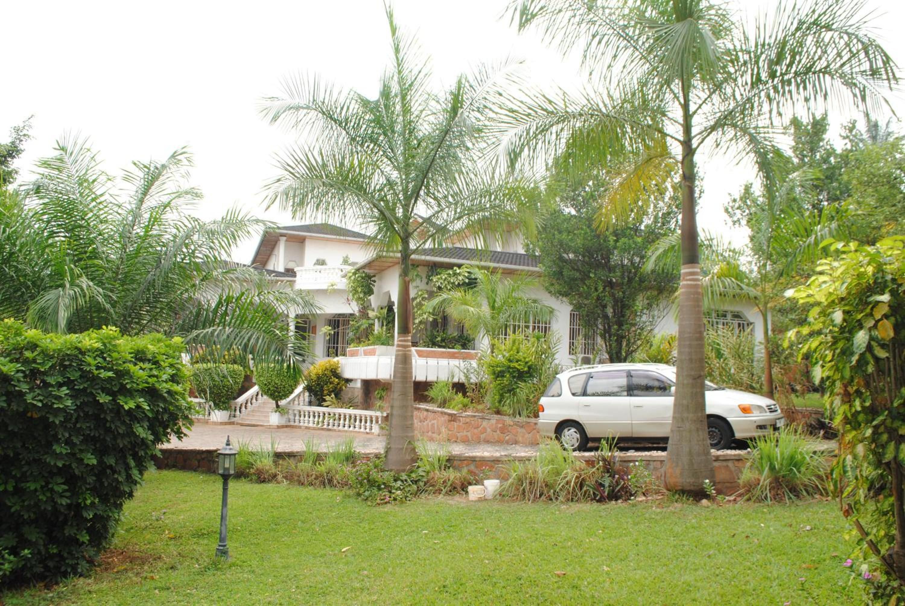 A residential area with a white car parked in front of a house with a balcony. There are palm trees and a well-maintained lawn.