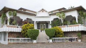 Un edificio de dos pisos con entrada central, paredes de piedra y un balcón con barandillas blancas.