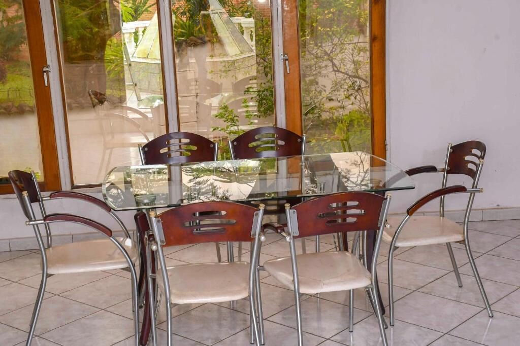 A dining area with a glass table and metal chairs, large windows, and a tiled floor.