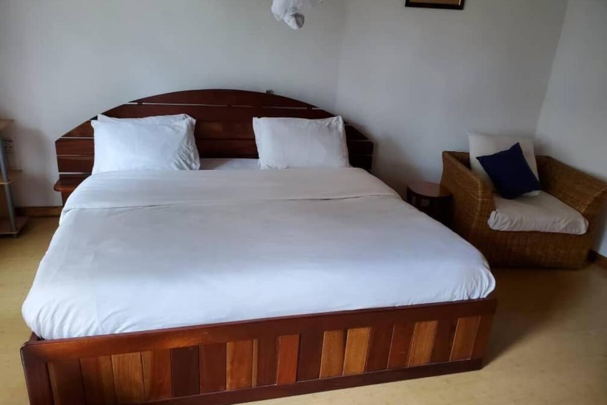 Ein großes Bett mit einem hölzernen Kopfteil, ein Sessel mit Kissen und ein kleiner Tisch.