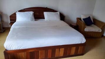 A large bed with a wooden headboard, a chair with a cushion, and a small table.