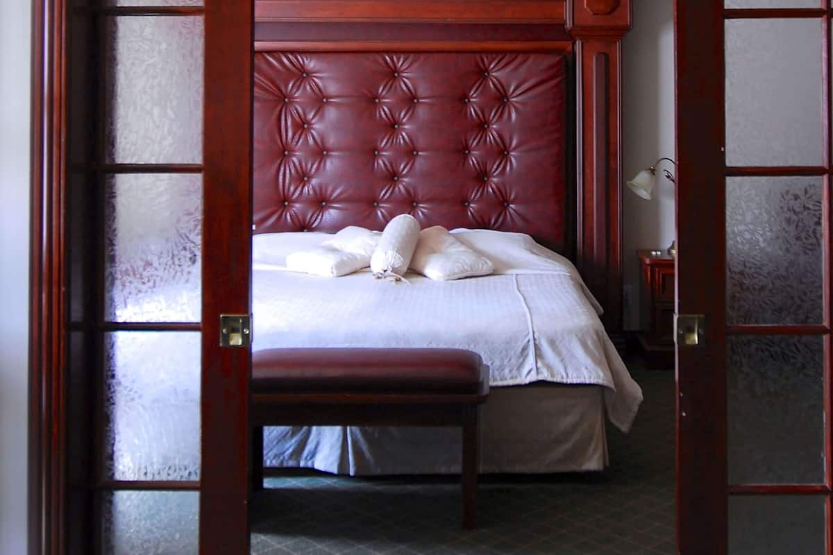 A bedroom with a tufted headboard, a bed with white linens, a bench, and a nightstand with a lamp.
