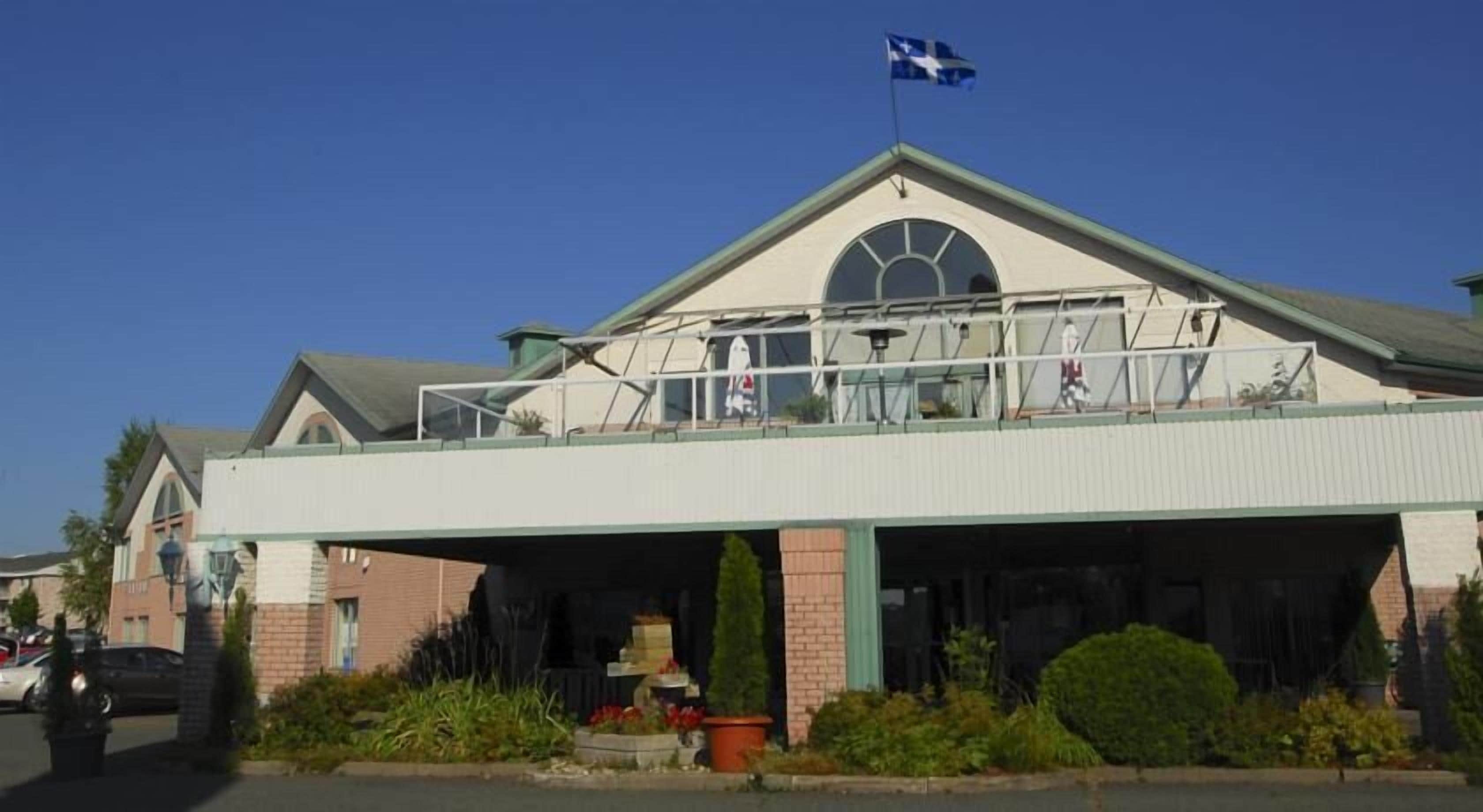 A building with a covered entrance, a flag on top, and a balcony with railings.