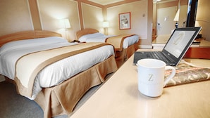 Hotellihuone, jossa on kaksi sänkyä, kannettava tietokone, kahvimuki ja peili.