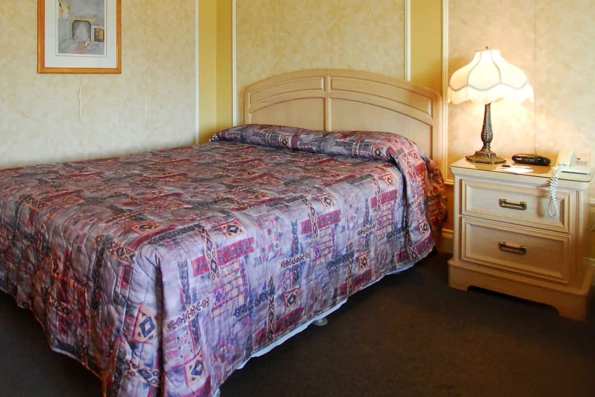 A neatly made bed with a patterned bedspread, a bedside lamp, and a nightstand with a telephone.