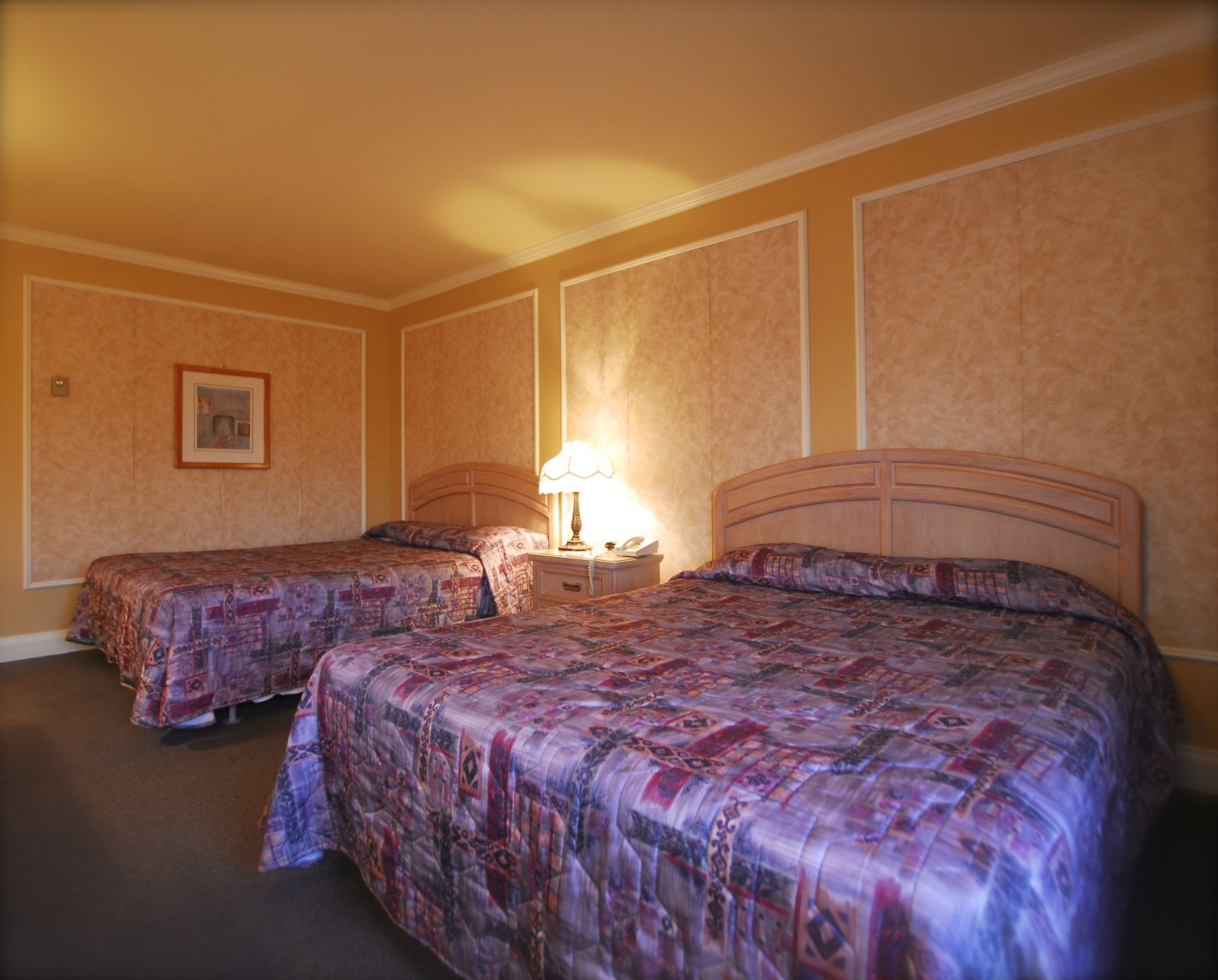 A hotel room with two beds, a nightstand with a lamp, and a framed picture on the wall.