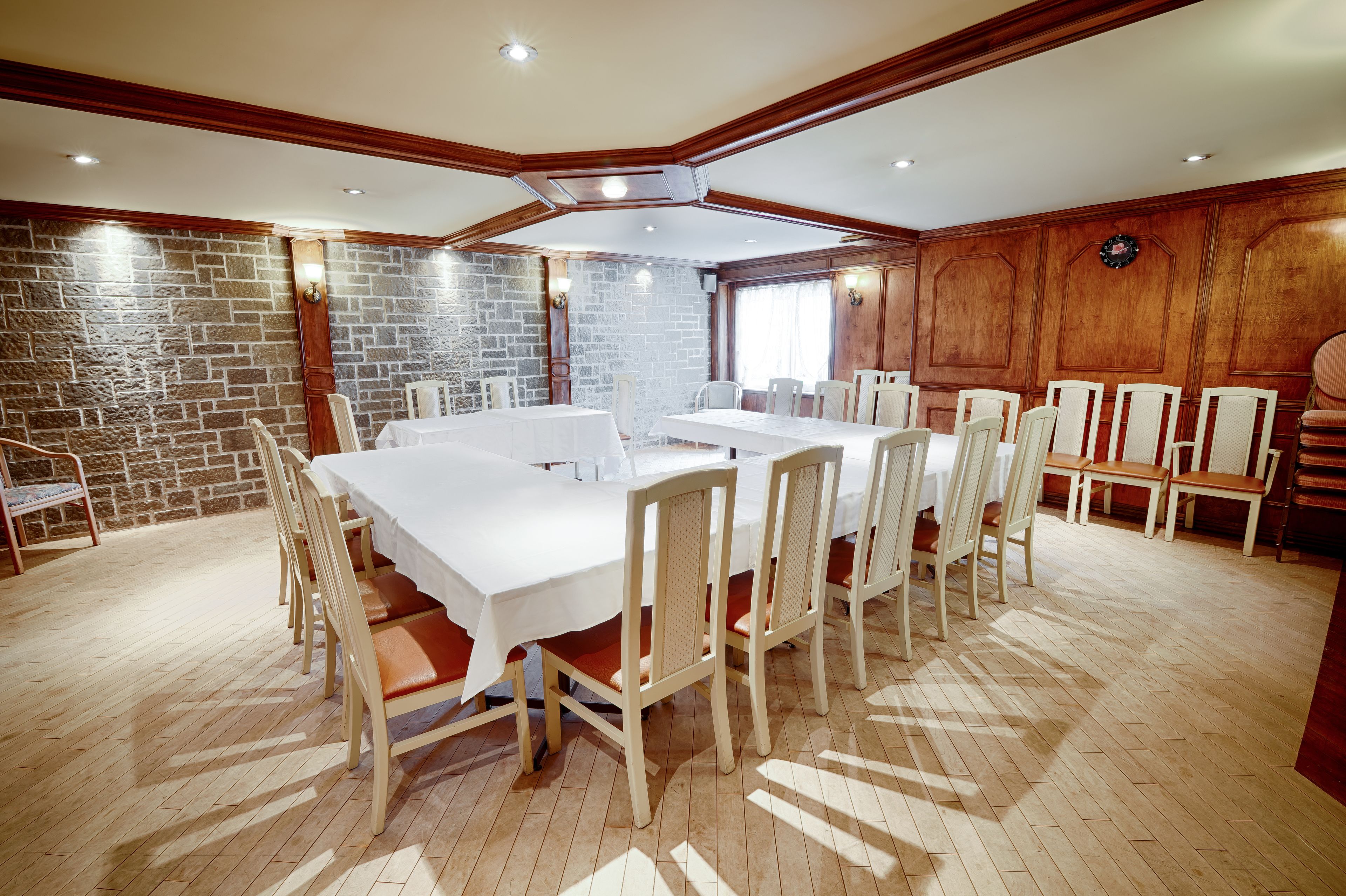 A conference room with a long table and chairs, wooden paneling, and a brick wall.