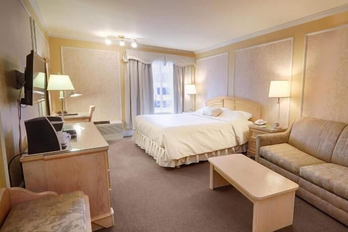 A hotel room with a bed, a sofa, a desk with a computer, a TV, and a bedside table.