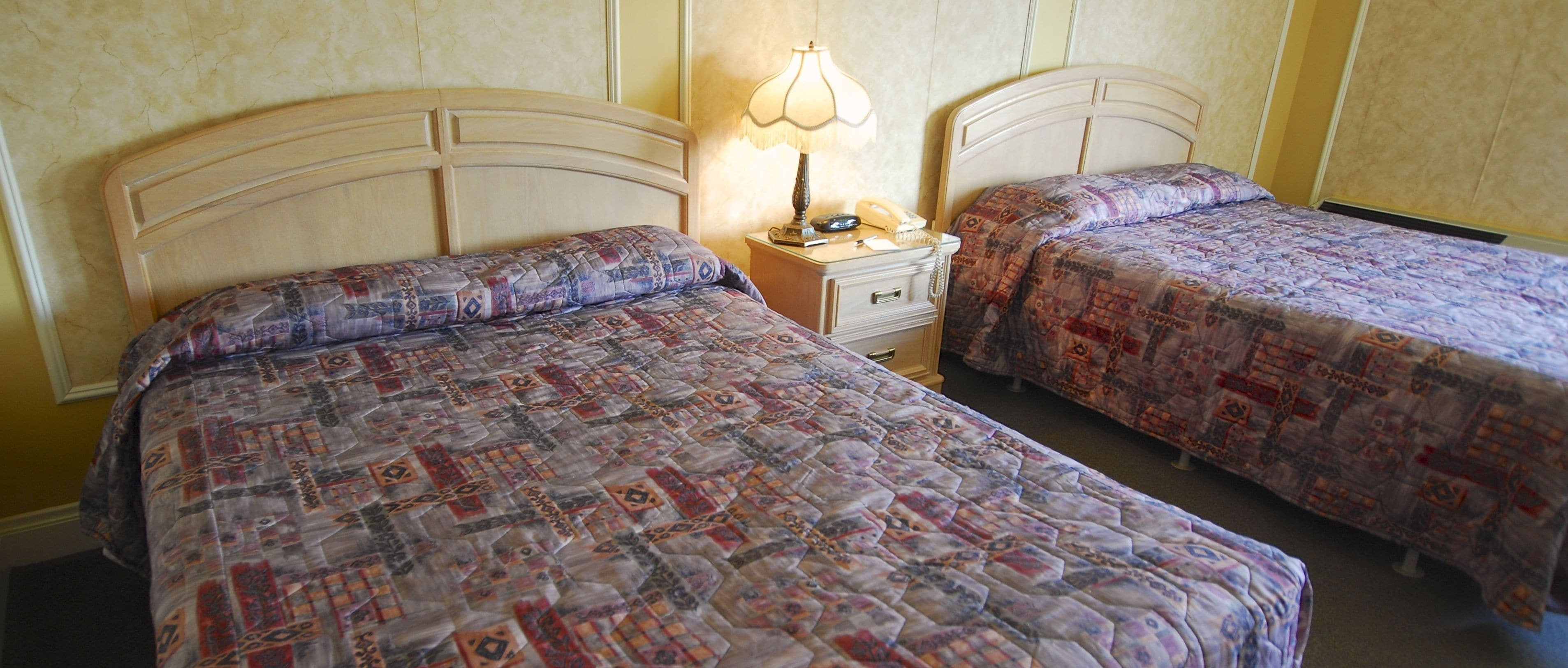 Dos camas individuales con colchas estampadas, una lámpara de noche y un teléfono sobre una mesita de madera.