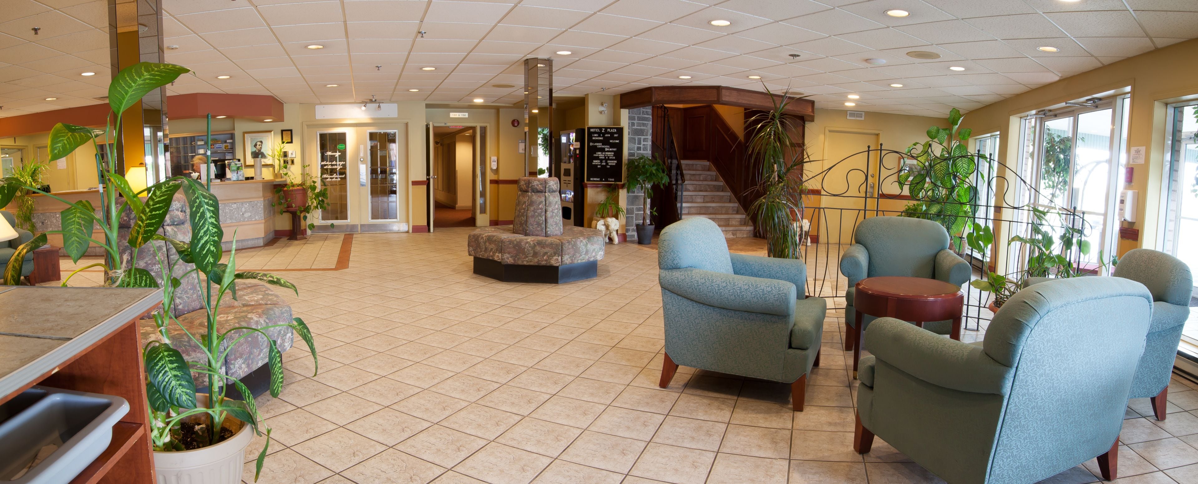 A spacious lobby with a central seating area, a staircase, and multiple potted plants.