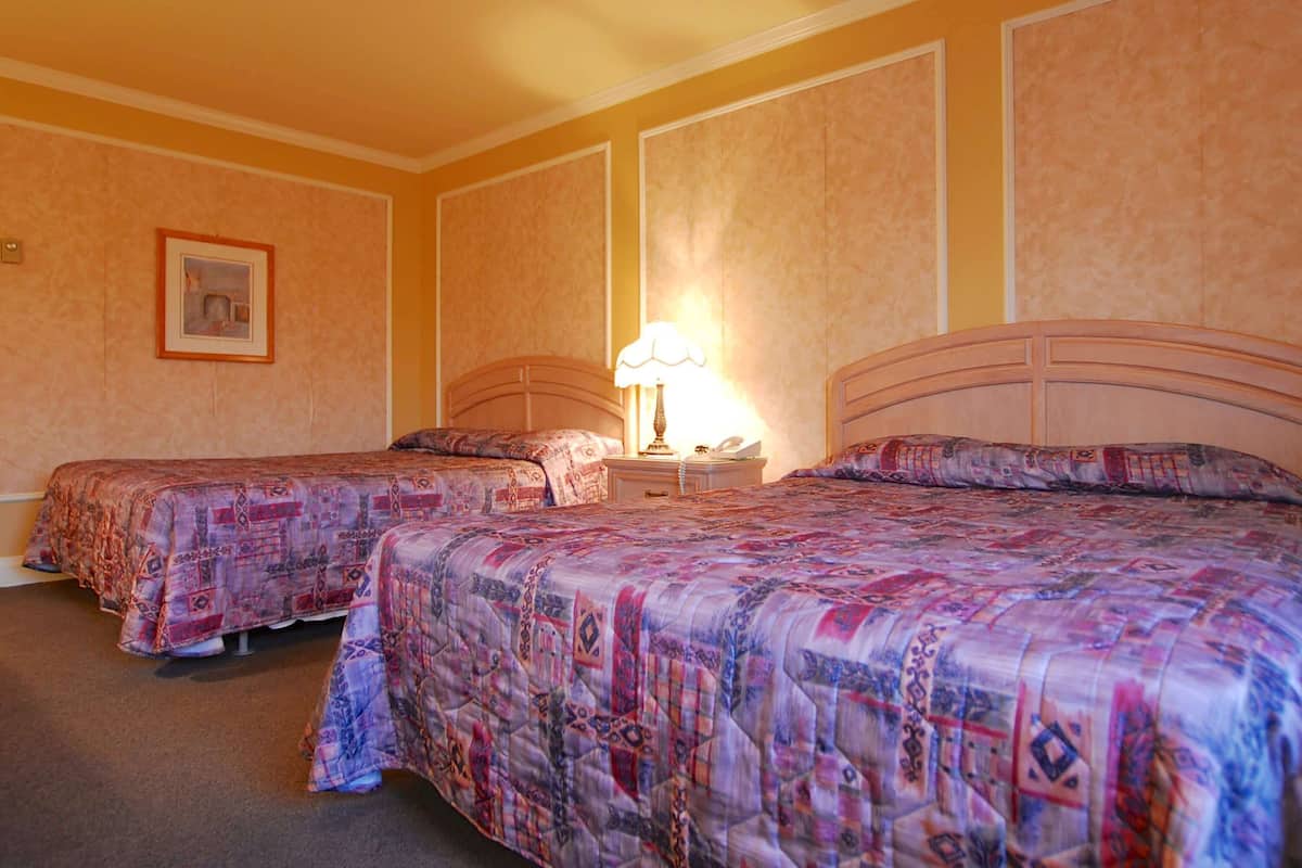A hotel room with two beds, a bedside table with a lamp, and a framed picture on the wall.