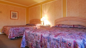 A hotel room with two beds, a bedside table with a lamp, and a framed picture on the wall.