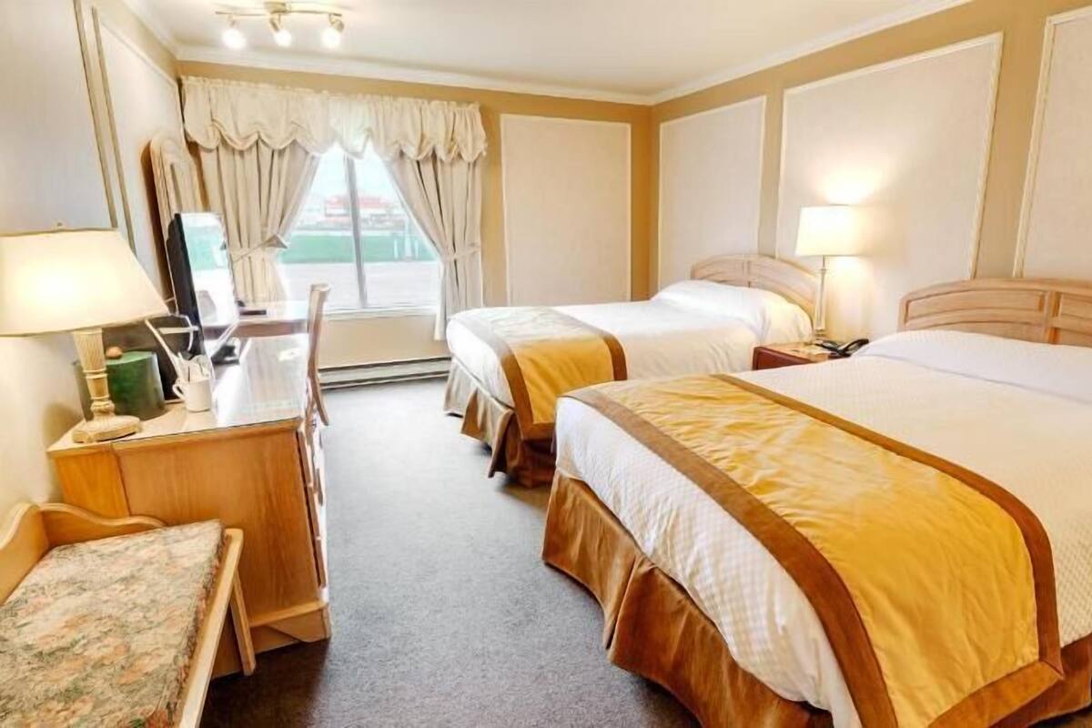 Une chambre d’hôtel avec deux lits, un bureau avec une lampe, une chaise et une fenêtre avec des rideaux.