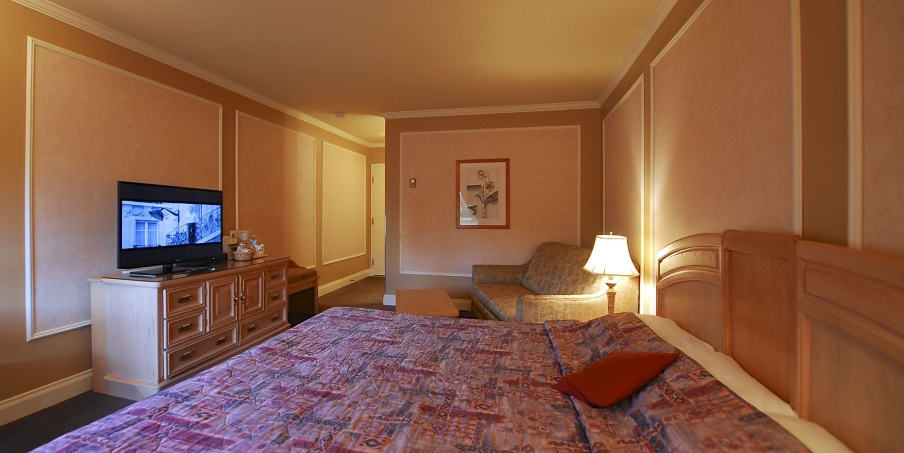 A hotel room with a large bed, a television on a dresser, a chair, and a lamp.