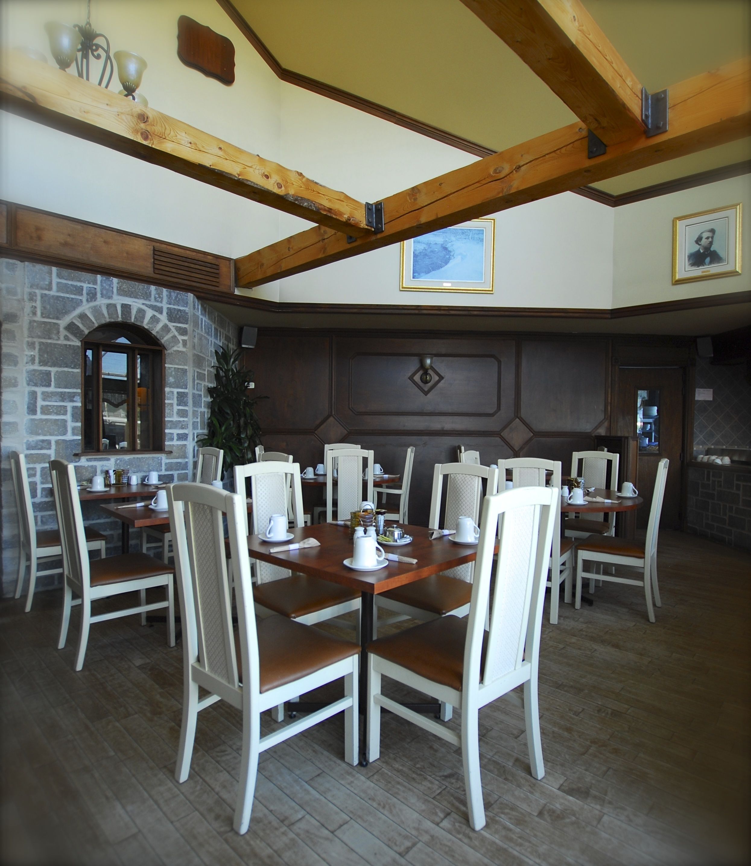 A dining area with wooden tables and white chairs, stone walls, and a fireplace.